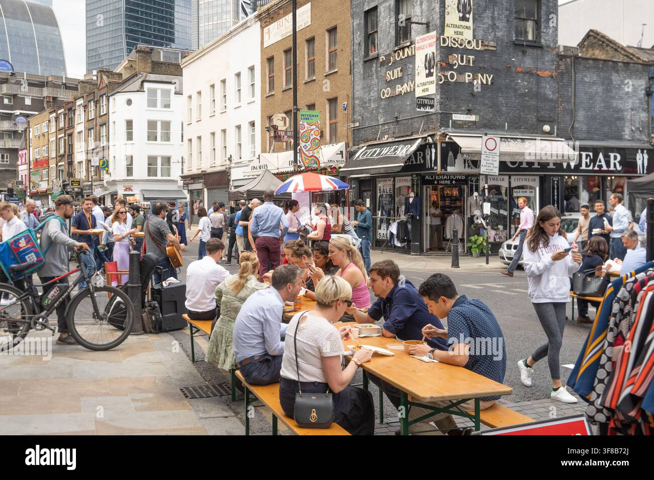 I dipendenti dell'ufficio godono del pranzo al vivace Petticoat Lane Market ad Aldgate, Londra, vicino all'incrocio con Bell Lane. Foto Stock