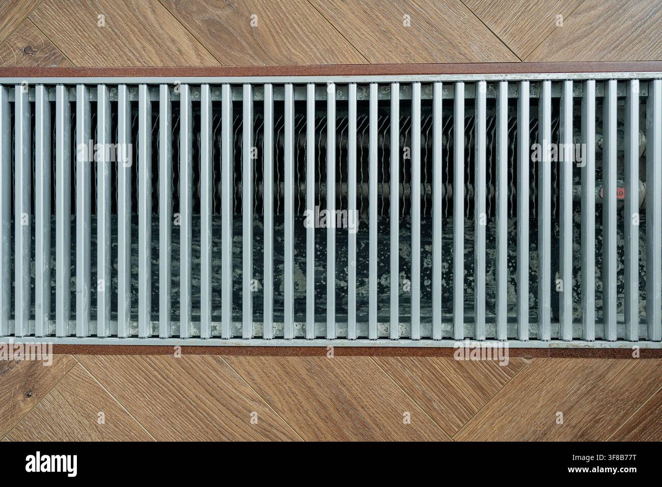 Vista dall'alto di una griglia di convettore a canalina in alluminio moderna integrata nel pavimento in parquet. Foto stock ideale per sistemi di riscaldamento moderni Foto Stock