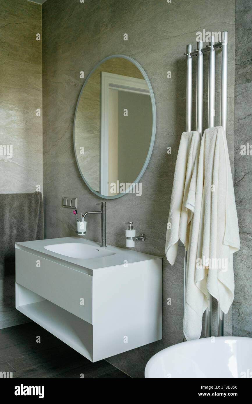 Armadietto sospeso bianco per lavandino con specchio rotondo e moderno asciuga asciugamani cromata appesa in un bagno piastrellato. Immagine perfetta per il design degli interni Foto Stock