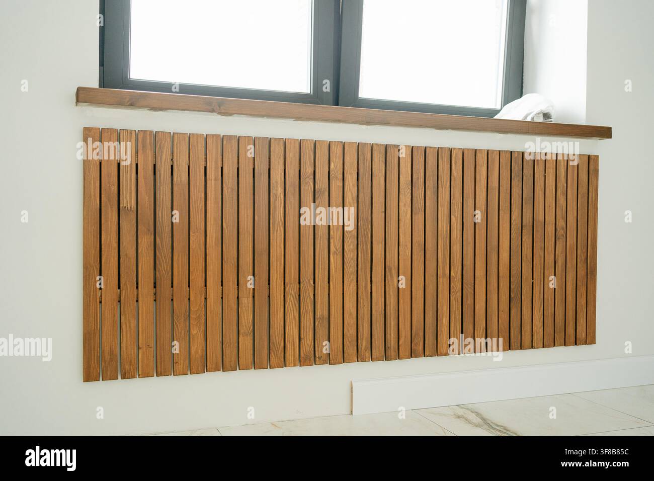Prima di lati verticali in legno che mascherano un sistema di riscaldamento sotto una finestra. Ottima risorsa visiva per l'architettura d'interni, design della falegnameria, riscaldamento Foto Stock