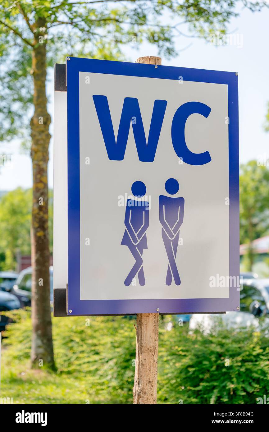 Primo piano di un cartello di servizi igienici all'aperto che mostra un uomo e una donna che tengono le gambe insieme su un palo di legno. Immagine stock perfetta per festival all'aperto Foto Stock