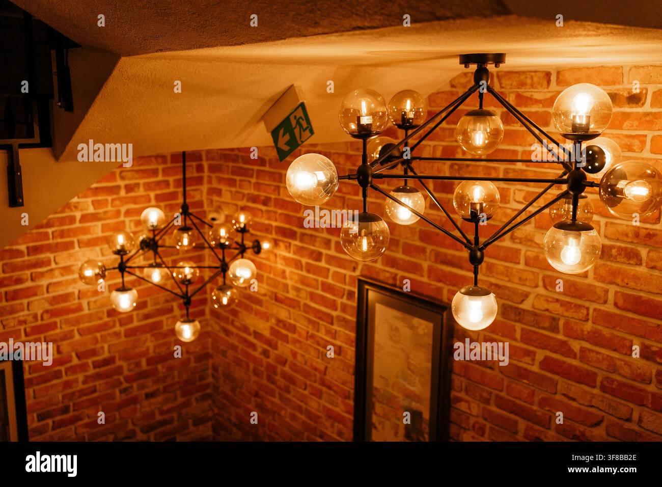 Eleganti lampade a sospensione geometriche che brillano sopra una scala in legno con muro di mattoni. Immagine stock perfetta per gli interni moderni di caffè, stile industriale Foto Stock