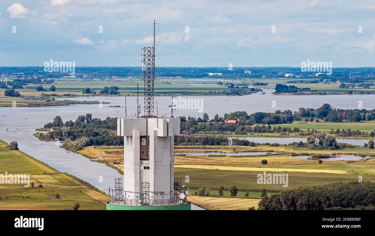 Veduta aerea della torre di telecomunicazioni e centro dati ViaData Toren che si erge sopra il paesaggio piatto e verde, i canali sinuosi e i campi agricoli Foto Stock