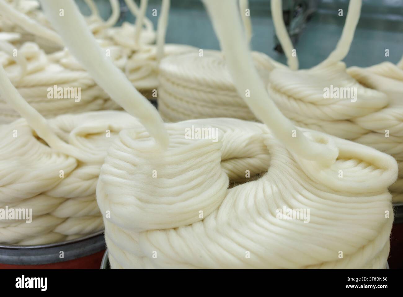 Vista ravvicinata di filamenti di morbida lana merino avvolti in bobine all'interno di una fabbrica tessile, che illustra la fase di preparazione alla filatura del filo di lana industriale Foto Stock