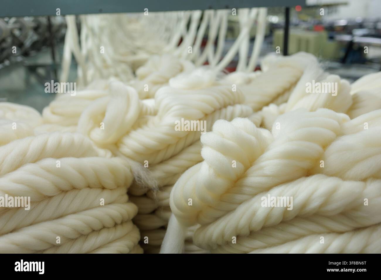 Vista ravvicinata di filamenti di lana merino attorcigliati che formano filati voluminosi all'interno di una linea di filatura di una fabbrica tessile, adatta per illustrare la lavorazione della lana, fornitura Foto Stock