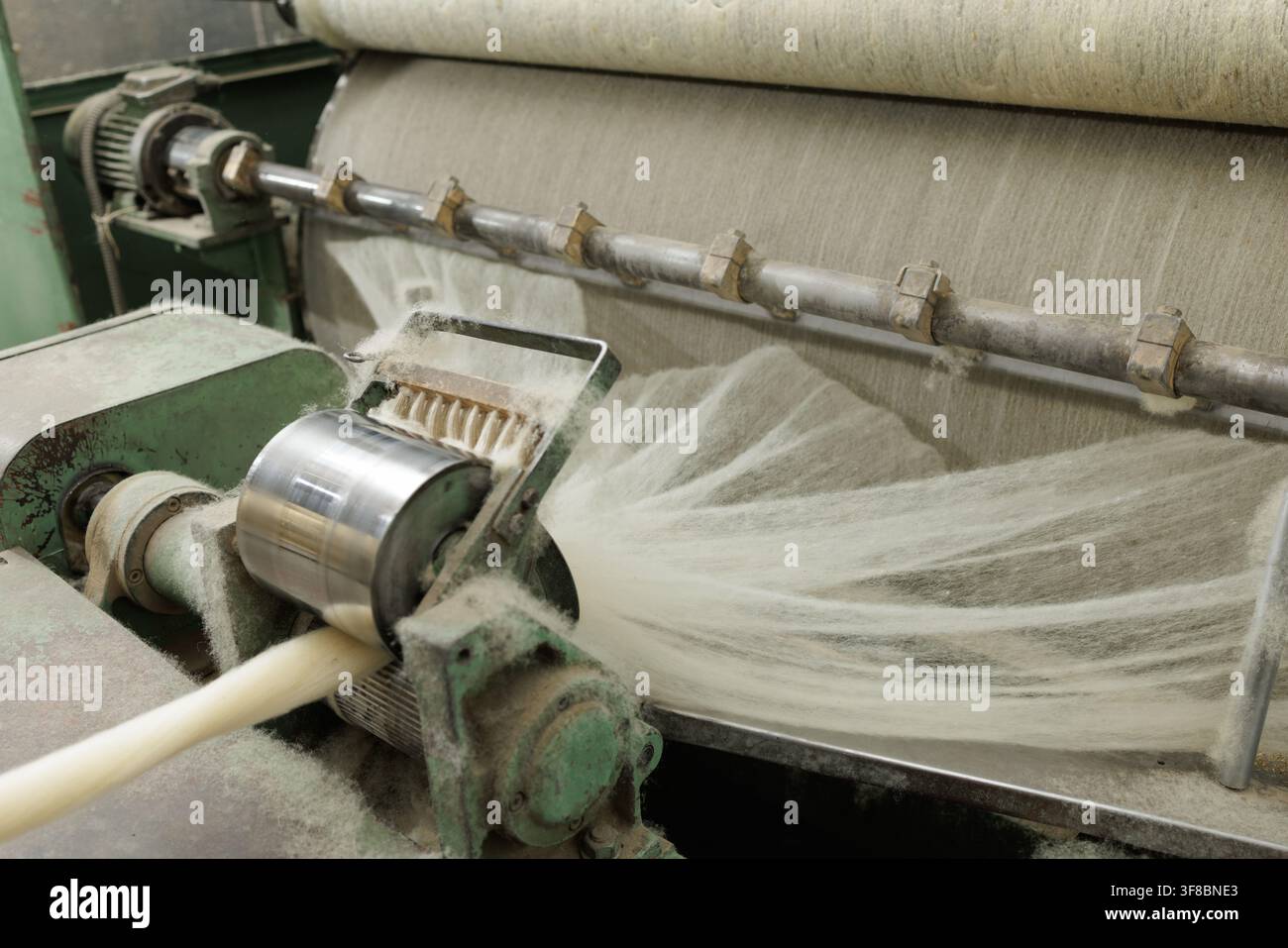 Macchina di cardatura industriale che elabora sottili filoni di lana merino in una filatura, mostrando la preparazione automatizzata delle fibre per la produzione di filati in un tessile Foto Stock