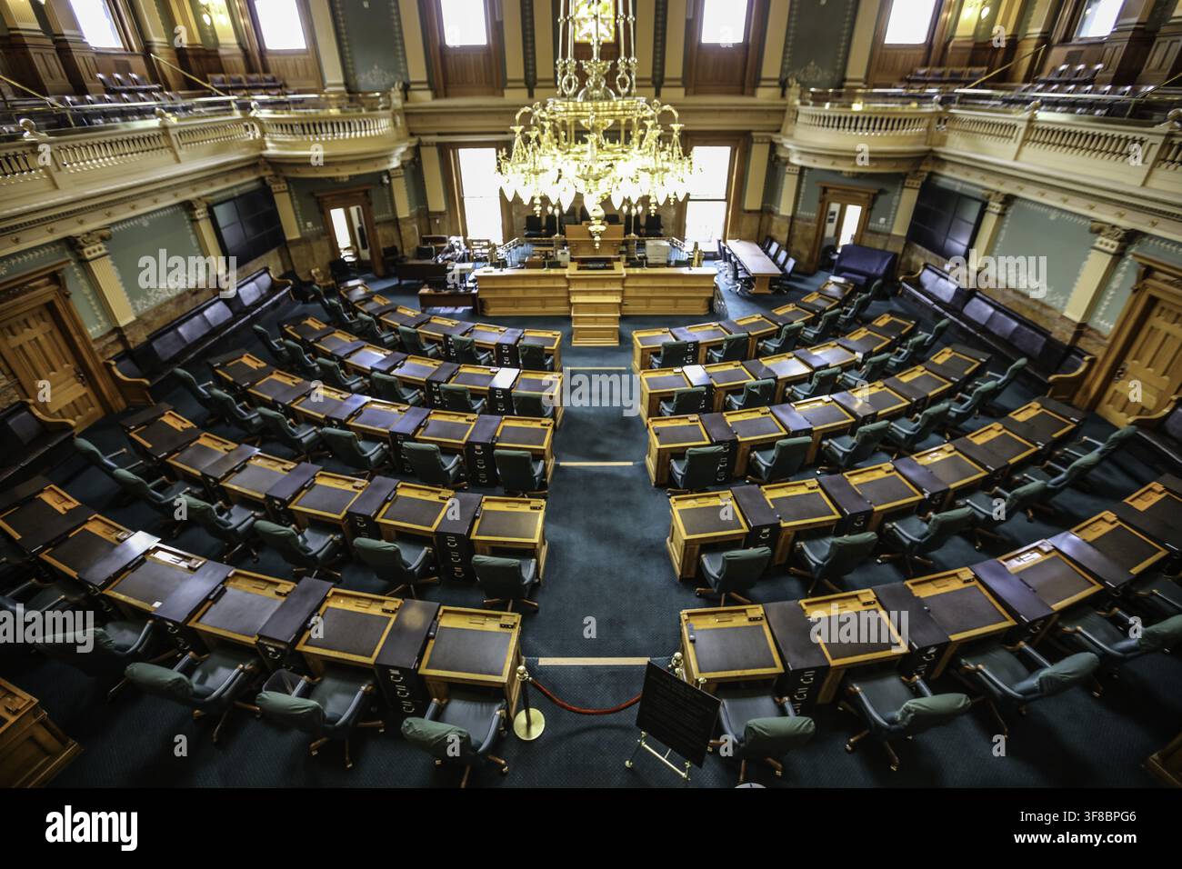 Vista della camera legislativa all'interno del Colorado State Capitol con file di scrivanie in legno, sedie verdi e un lampadario ornato a Denver, Foto Stock