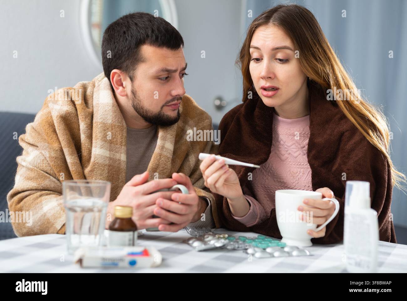 Coppia affetta da influenza e tosse seduta avvolta in coperte Foto Stock