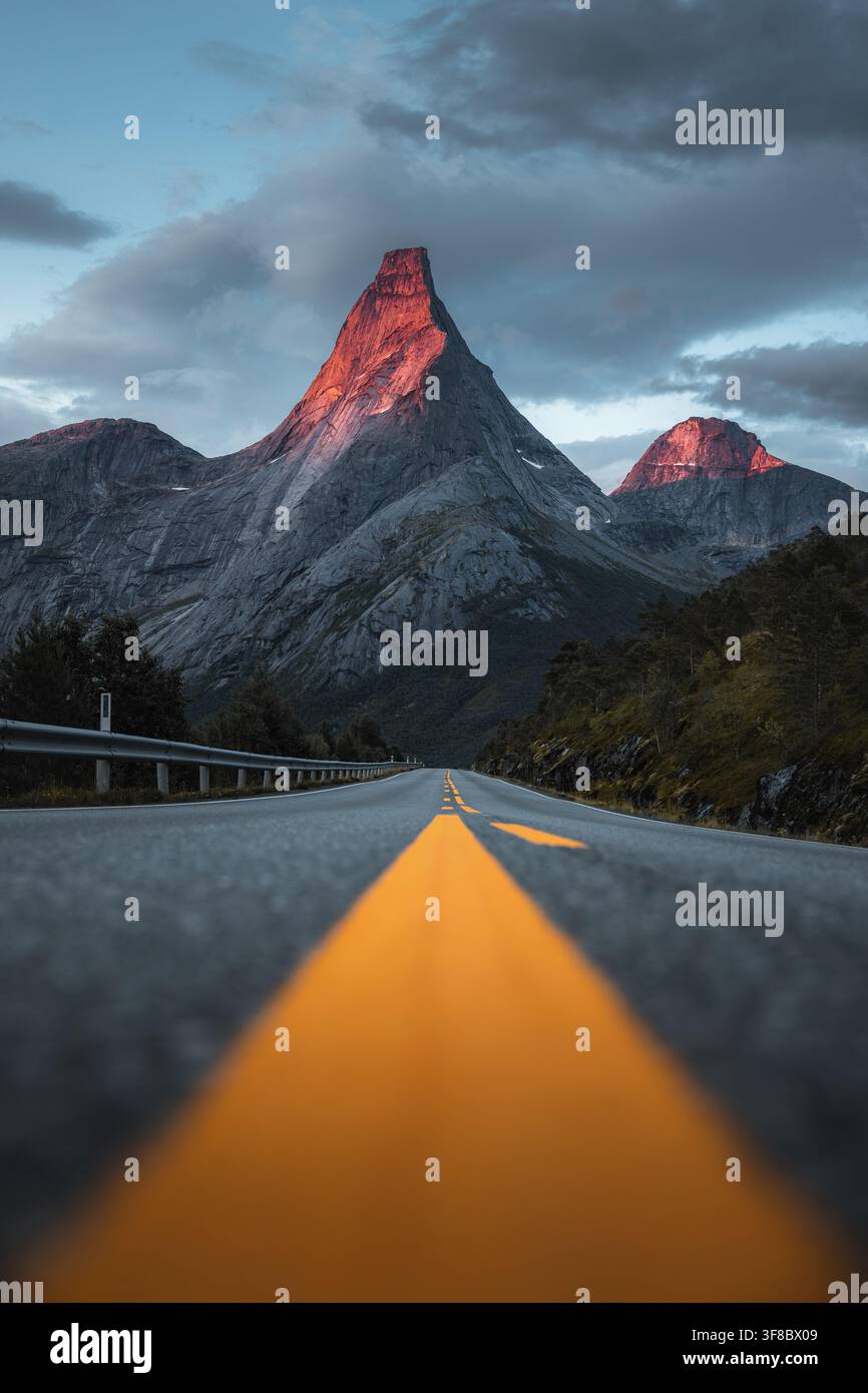 Vista dell'iconica montagna Stetind illuminata dalla luce dorata del tramonto alla fine di una strada asfaltata tortuosa nel comune di Narvik, Nordland, Norvegia. Foto Stock