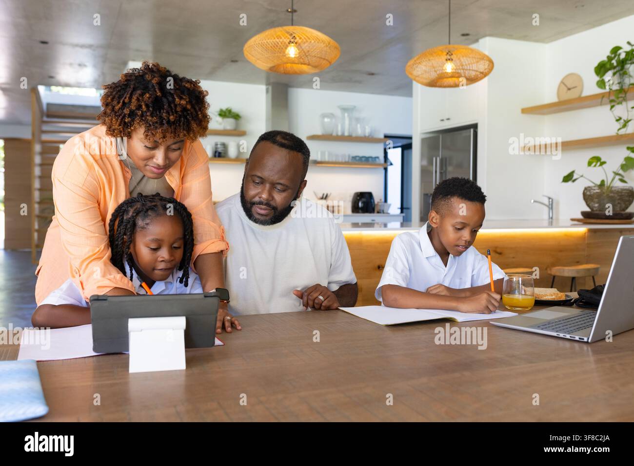 Famiglia afroamericana che aiuta la figlia su un supporto per tablet mentre i bambini in camicie bianche scrivono al PC Foto Stock