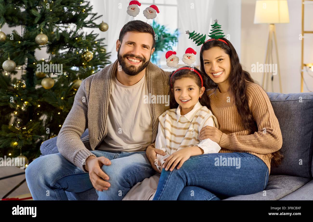 Allegro ritratto di famiglia con la figlia sul divano che indossa divertenti cerchietti natalizi Foto Stock