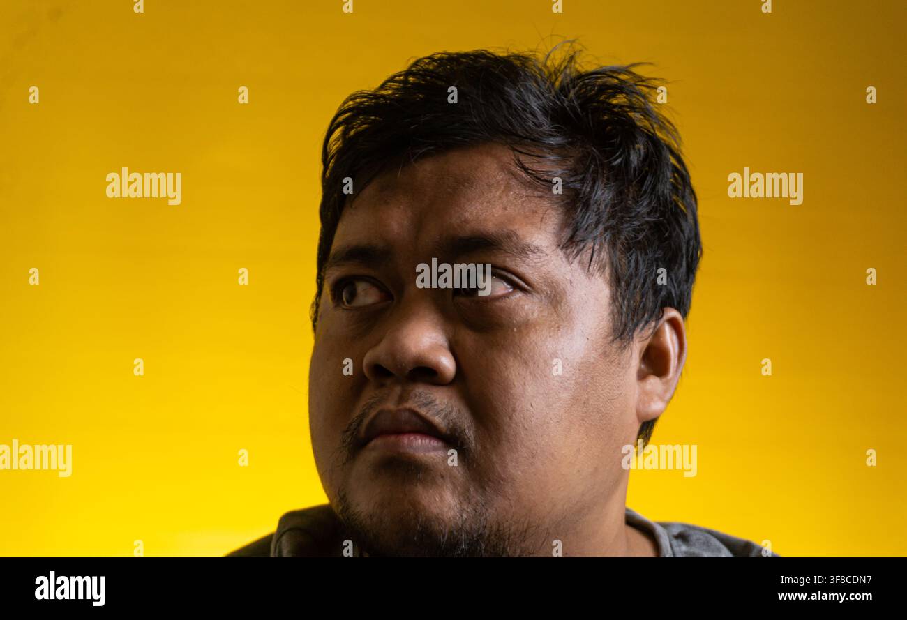 Ritratto ravvicinato di un giovane uomo asiatico che guarda di lato con un'espressione facciale seria, leggermente preoccupata e contemplativa. Il soggetto ha Foto Stock
