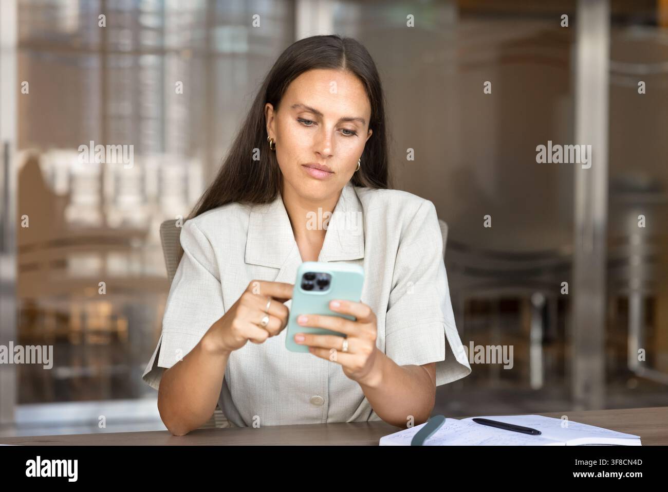 Donna d'affari caucasica adulta che controlla i messaggi su uno smartphone in ufficio Foto Stock