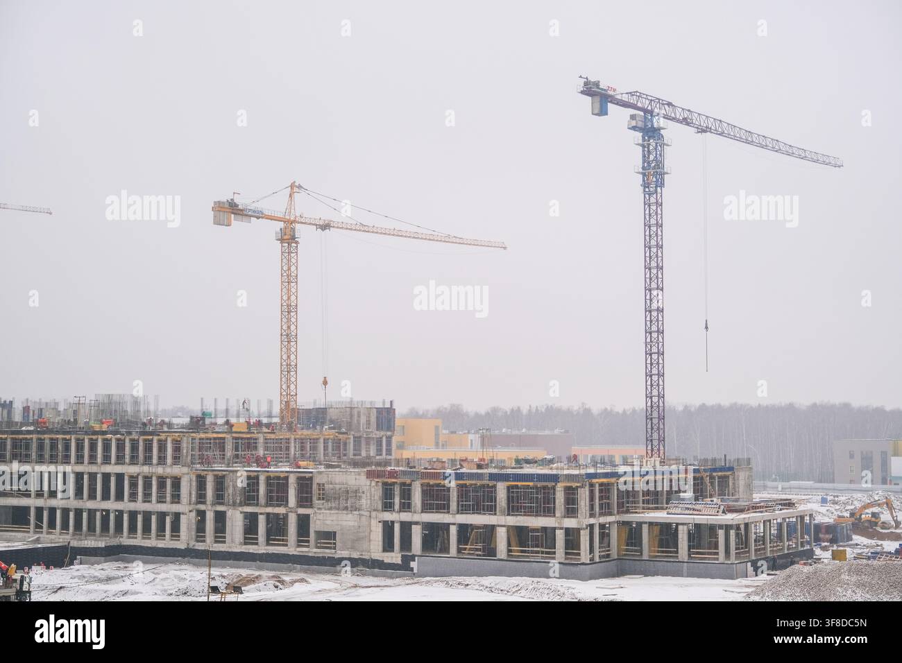 Mosca, Russia, 03.03.2025 Grande cantiere edile con edifici incompiuti e due gru torreggianti sotto un cielo nuvoloso con neve invernale per sviluppo Foto Stock