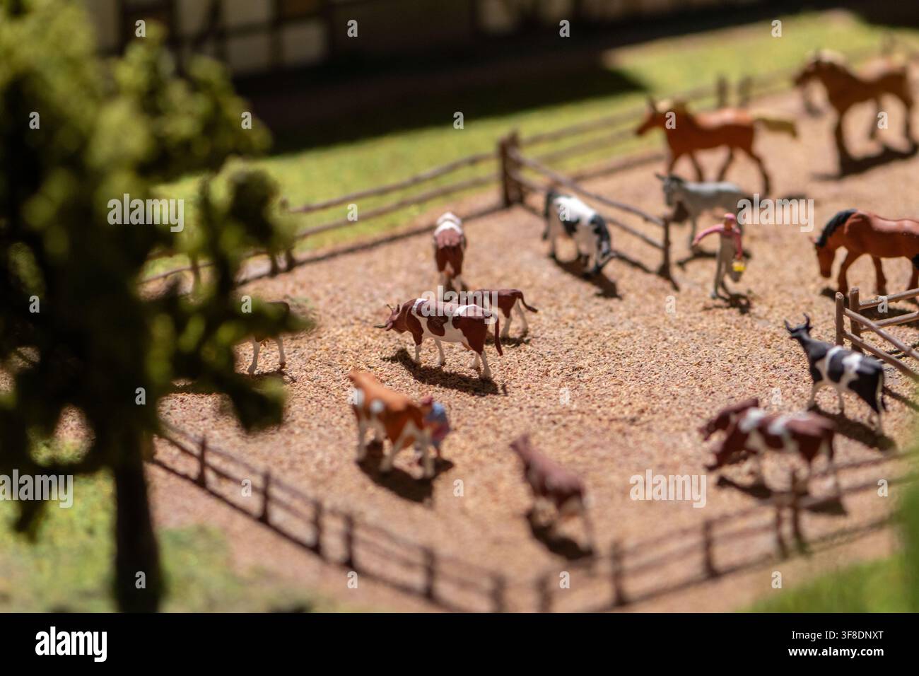Un primo piano a fuoco poco profondo mostra un diorama in miniatura di una fattoria con mucche, cavalli, recinti, alberi e una piccola figura di contadino. Foto Stock