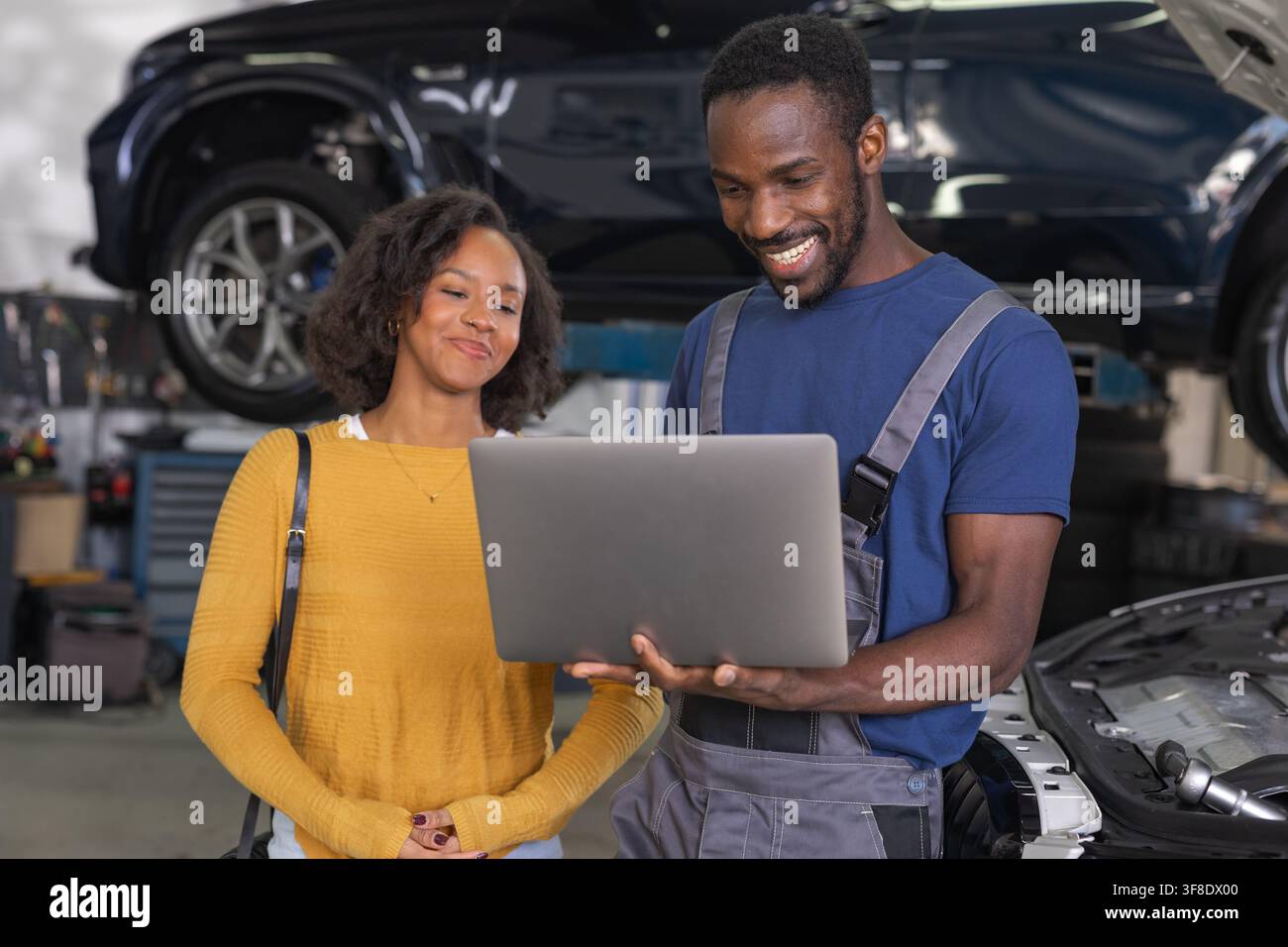 Meccanico professionista in officina che utilizza un laptop per la diagnostica moderna dei veicoli, mostrando alla cliente i dati del motore della sua auto. Foto Stock