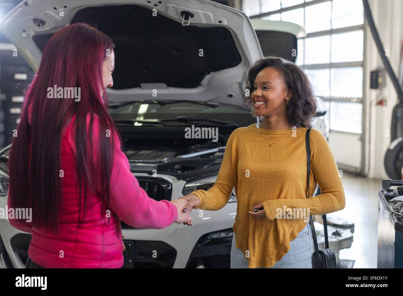 Tecnica che stringe la mano e consegna le chiavi dell'auto a un cliente soddisfatto dopo un servizio di riparazione e diagnostica automobilistica riuscito. Foto Stock