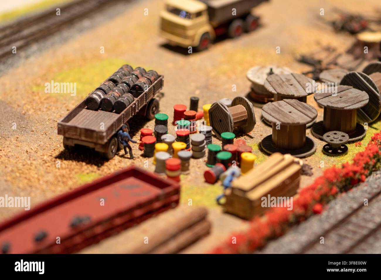 Una vista ravvicinata di un diorama industriale in miniatura mostra un rimorchio a pianale carico di barili accanto a tamburi sparsi, bobine di cavo e minuscoli operai fi Foto Stock