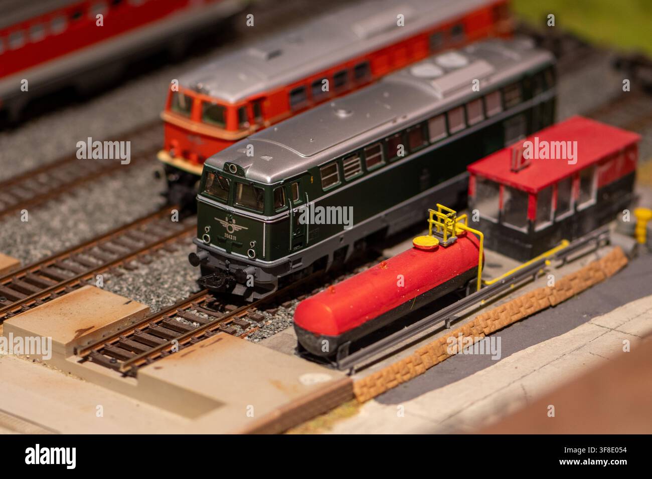 Una vista ravvicinata mostra locomotive diesel in miniatura su un layout dettagliato di modellismo ferroviario accanto a un serbatoio di carburante rosso e una piccola struttura di servizio. Foto Stock