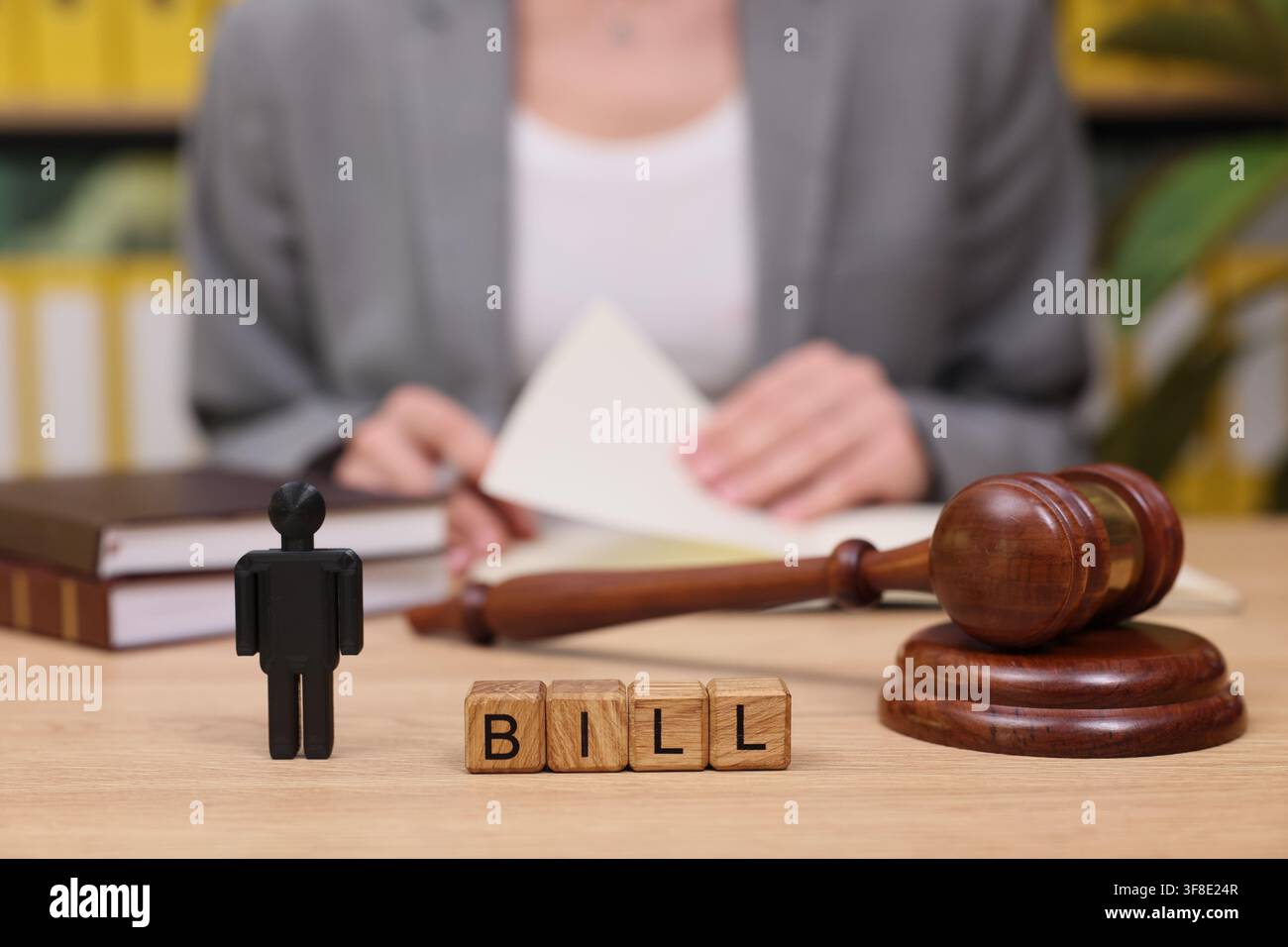 Le decisioni legali si svolgono mentre una figura si trova accanto a blocchi di legno che formano la parola "bill" in uno studio legale pieno di libri di diritto Foto Stock