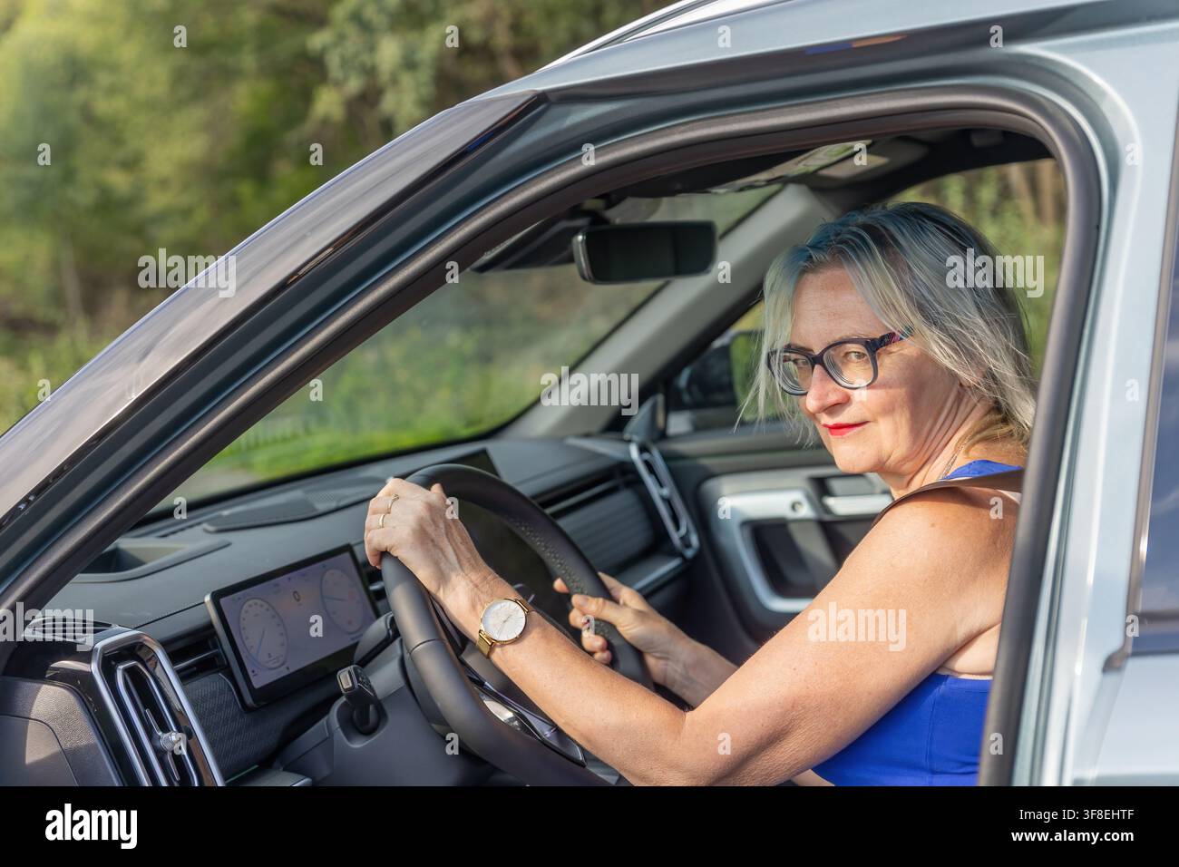 Donna sorridente di mezza età è seduta in una nuova auto moderna. Orizzontalmente. Foto Stock