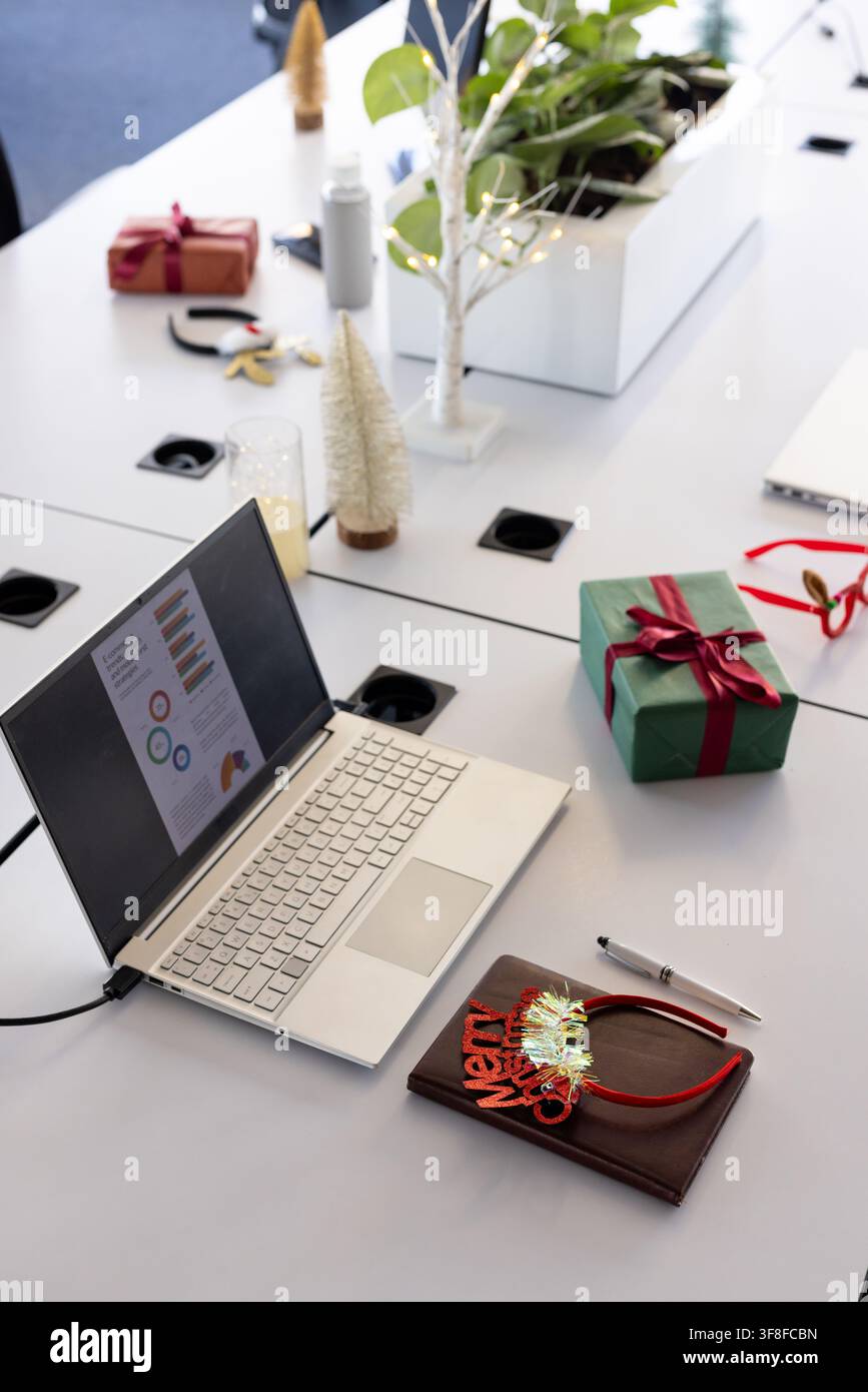 Laptop argentato mostra grafici colorati su tavolo modulare bianco in ufficio con regali Foto Stock