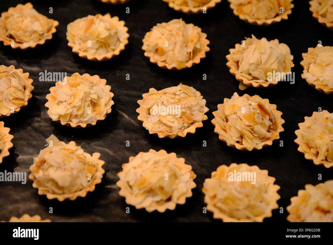 Vista ad angolo alto di mini crostate alle mandorle ricoperte di mandorle affettate disposte su uno sfondo nero. Foto Stock