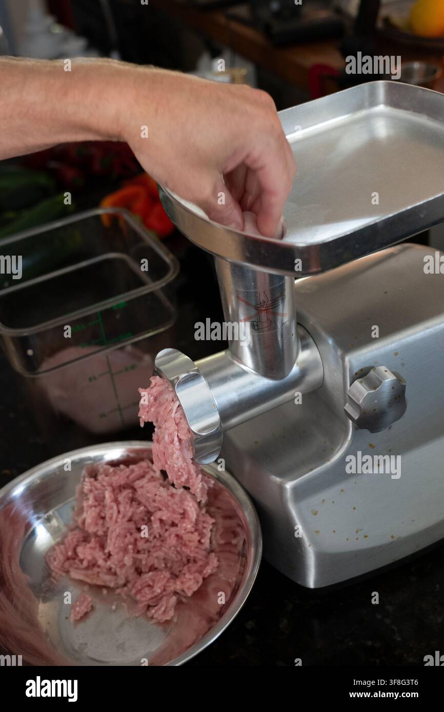 Persona che macina carne fresca con un tritacarne da banco in una cucina domestica Foto Stock
