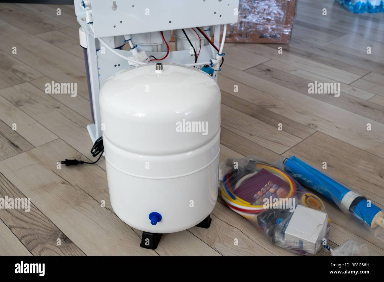 Serbatoio di espansione bianco per sistema di purificazione dell'acqua ad osmosi inversa posizionato sul pavimento accanto all'unità di filtrazione principale e agli accessori per l'installazione. Foto Stock