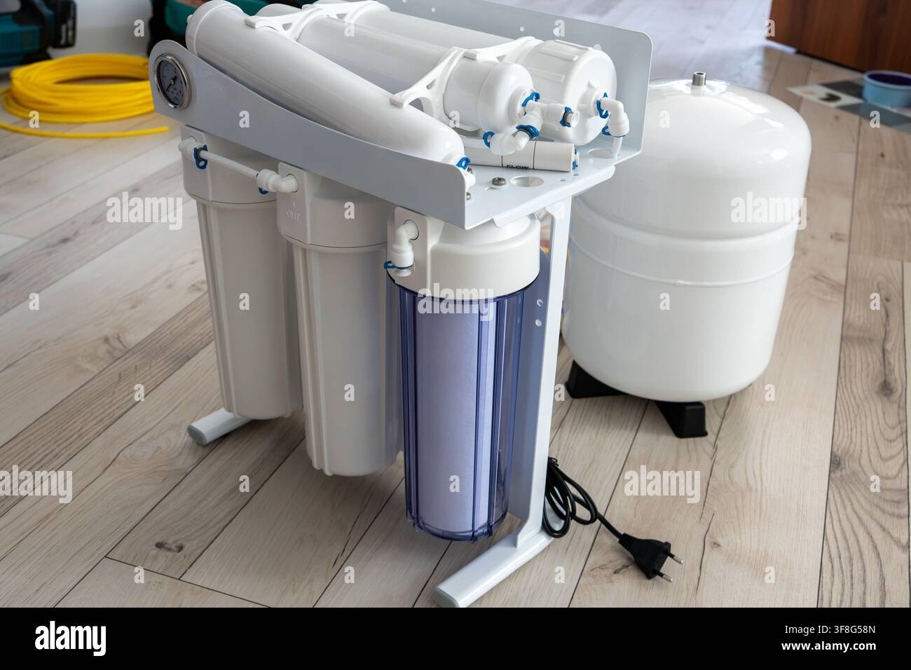 Sistema di purificazione dell'acqua a osmosi inversa domestico con cartucce di sedimenti verticali e serbatoio di metallo bianco in piedi su pavimento laminato prima di s Foto Stock