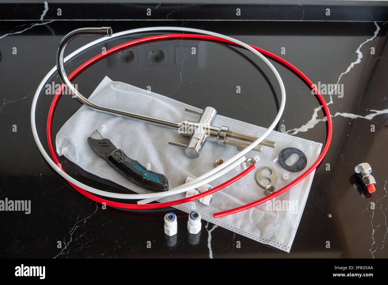 Meccanismo rubinetto cromato con tubi in plastica colorata, coltello multiuso e hardware di montaggio per sistema di filtraggio dell'acqua deposta su piano di lavoro in marmo nero Foto Stock