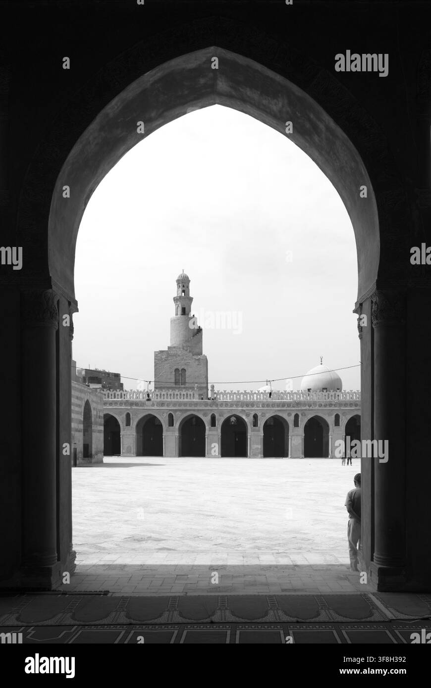 CAIRO, EGITTO: Il minareto a spirale del IX secolo della Moschea di Ibn Tulun incorniciato da un arco storico. Foto verticale in bianco e nero Foto Stock