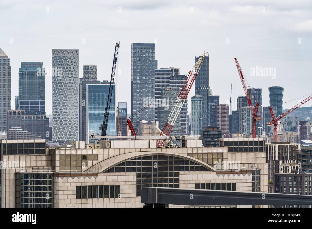 Vista della moderna skyline di Canary Wharf con numerosi grattacieli, facciate in vetro e gru edili sotto un cielo nuvoloso a Londra, Inghilterra, Unite Foto Stock