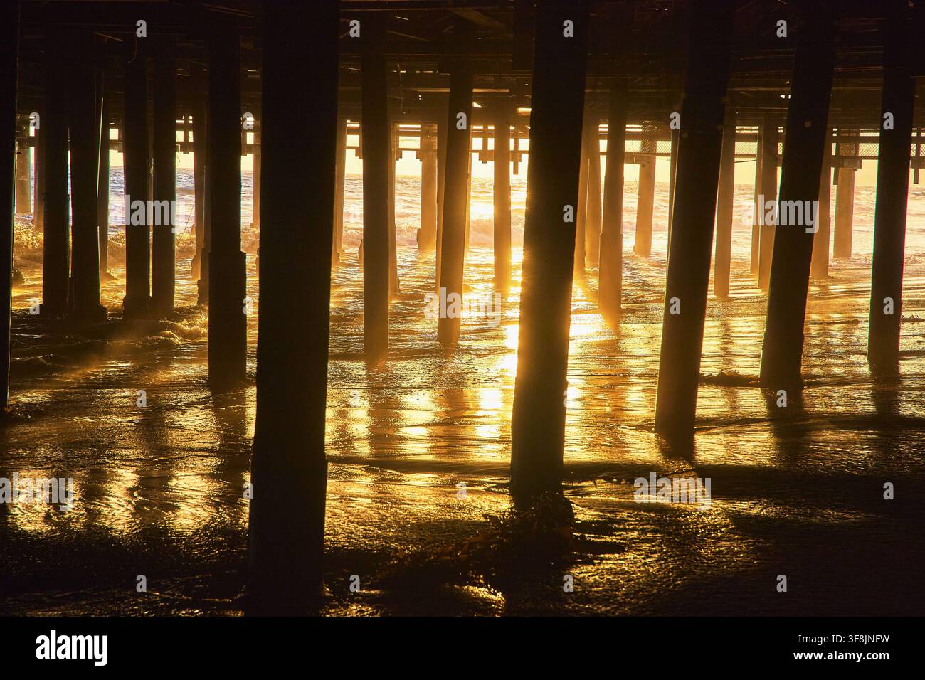 Luce dell'ora dorata sotto il molo di Santa Monica con riflessi sulla sabbia dell'oceano Foto Stock