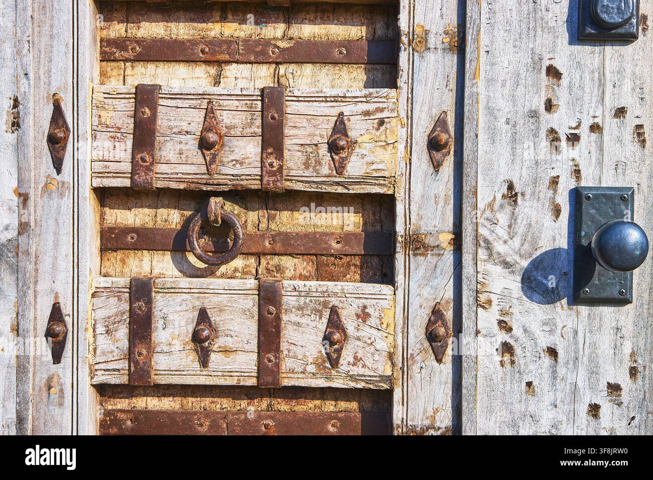 Primo piano di una porta di legno consumata con ferri e maniglia rustica ad anello Foto Stock