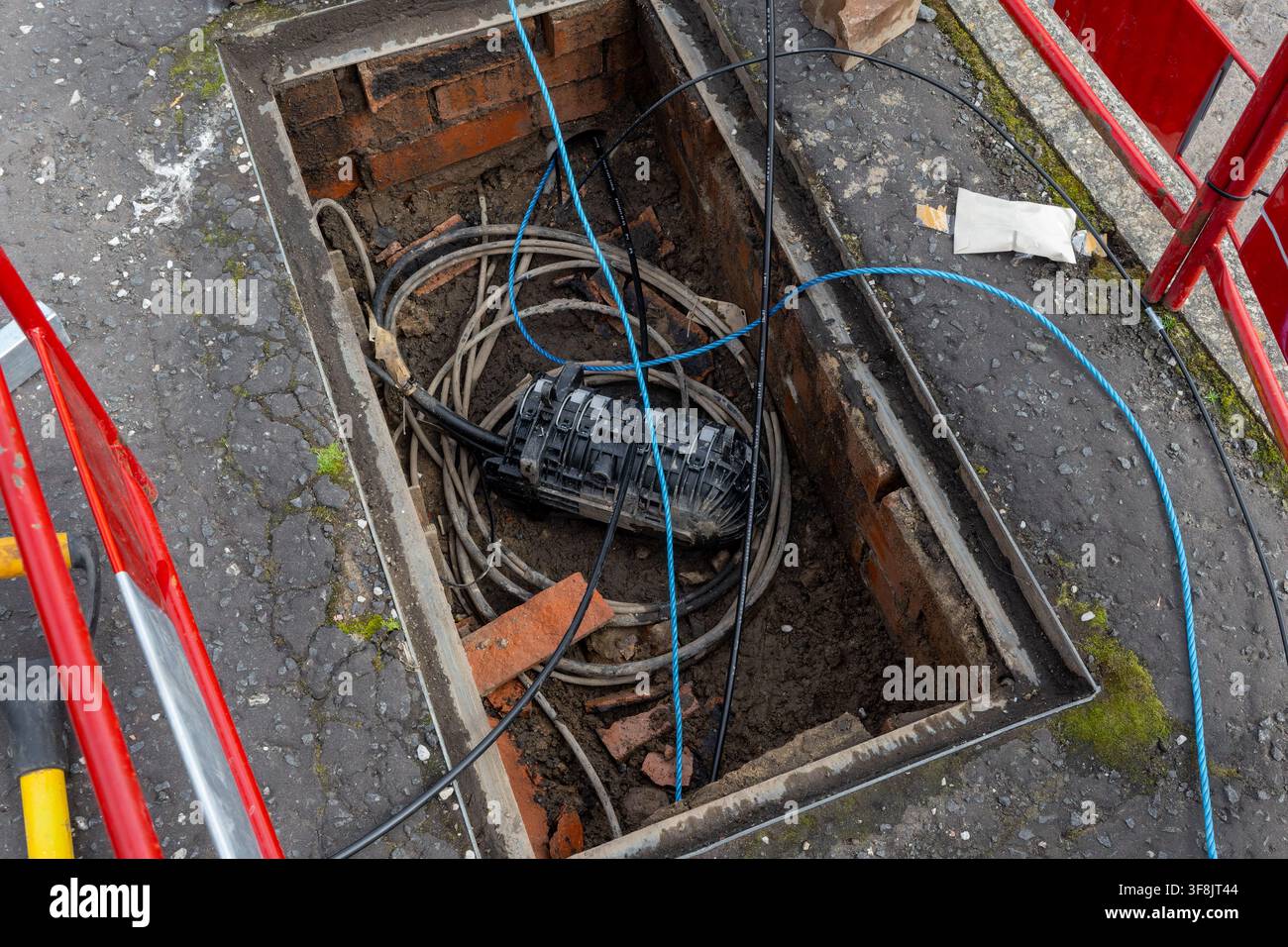Chiusura in fibra ottica nera si trova tra cavi arrotolati e corde di traino blu all'interno di una camera di telecomunicazioni aperta rivestita in mattoni. Barriere rosse e bianche incorniciano Foto Stock