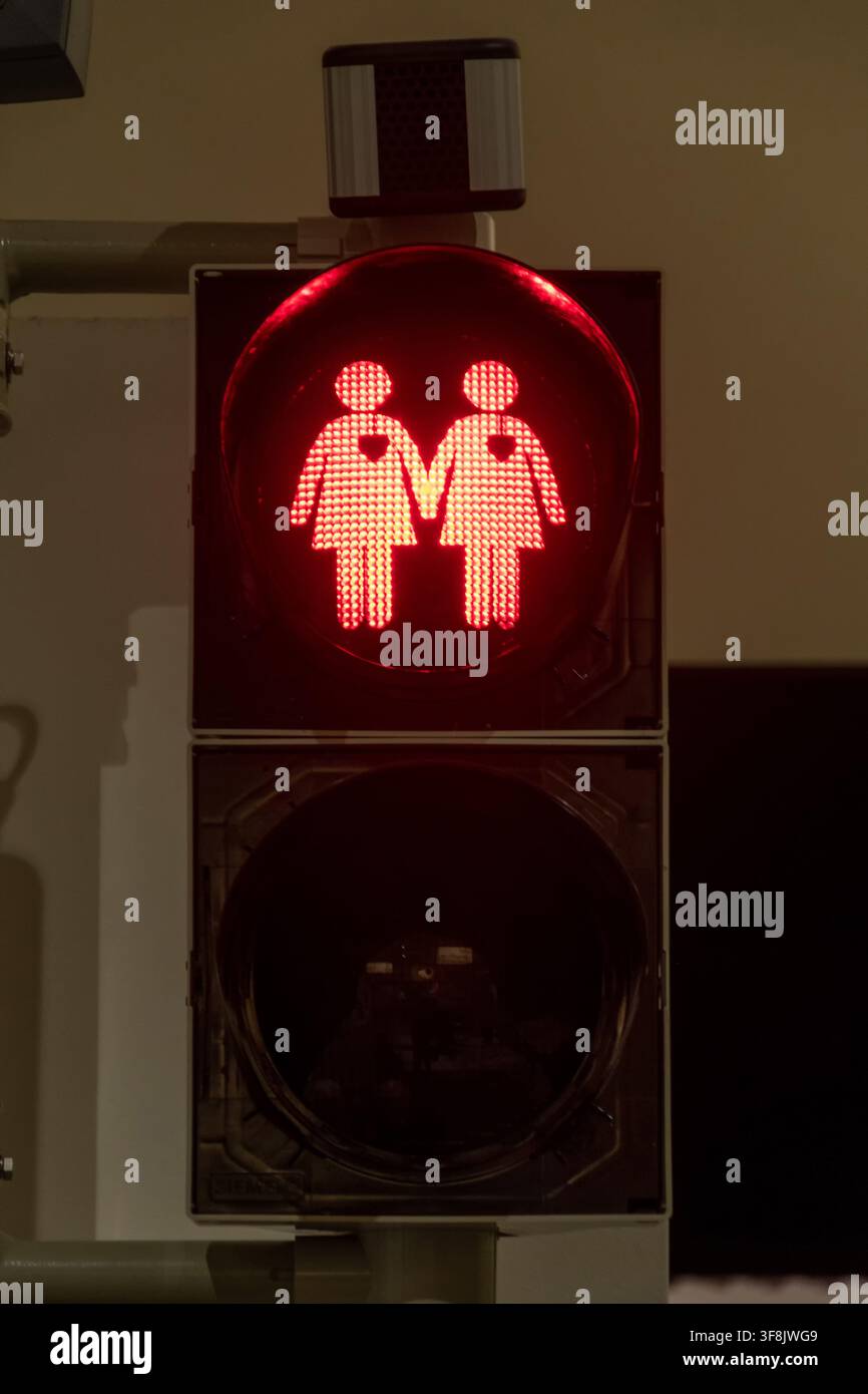 Un segnale stradale pedonale rosso mostra due figure femminili illuminate che si tengono per mano su uno sfondo scuro. Foto Stock