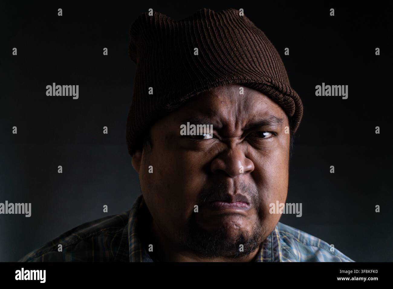 Un primo piano di un giovane uomo asiatico dell'Indonesia, nel Sud-est asiatico, che mostra un'espressione facciale arrabbiata su uno sfondo scuro, L'uomo indossa un Foto Stock