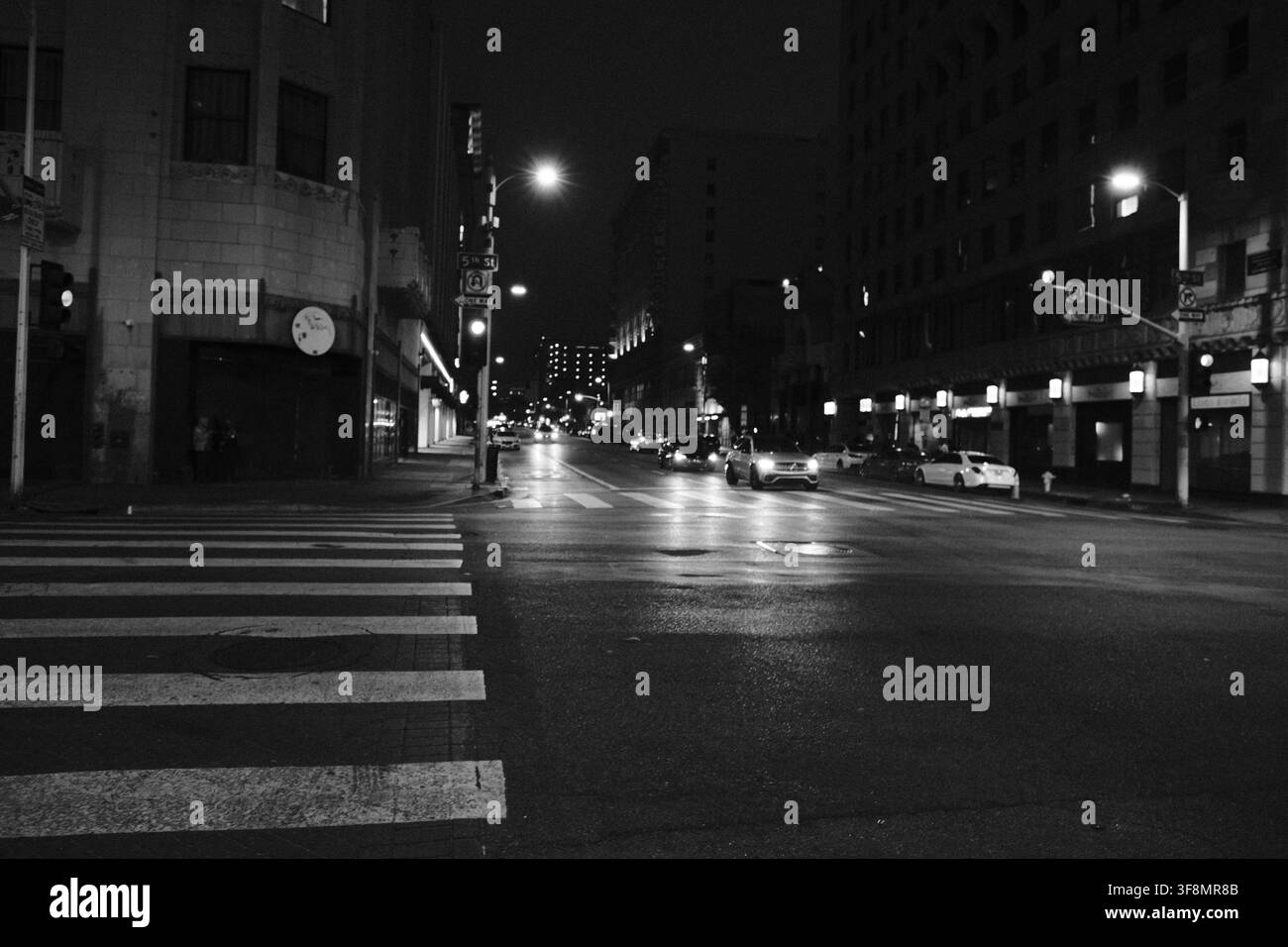 Incrocio del centro di Los Angeles di notte con attraversamenti pedonali, semafori e edifici illuminati, fotografato in bianco e nero. Foto Stock