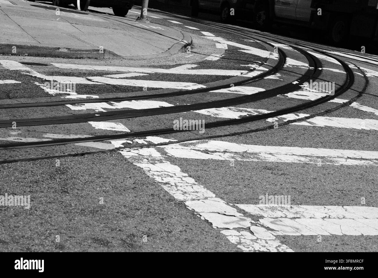 Binari curvi di funicolare attraversano segnaletica stradale dipinta a un incrocio di San Francisco, fotografati in bianco e nero ad alto contrasto. Foto Stock