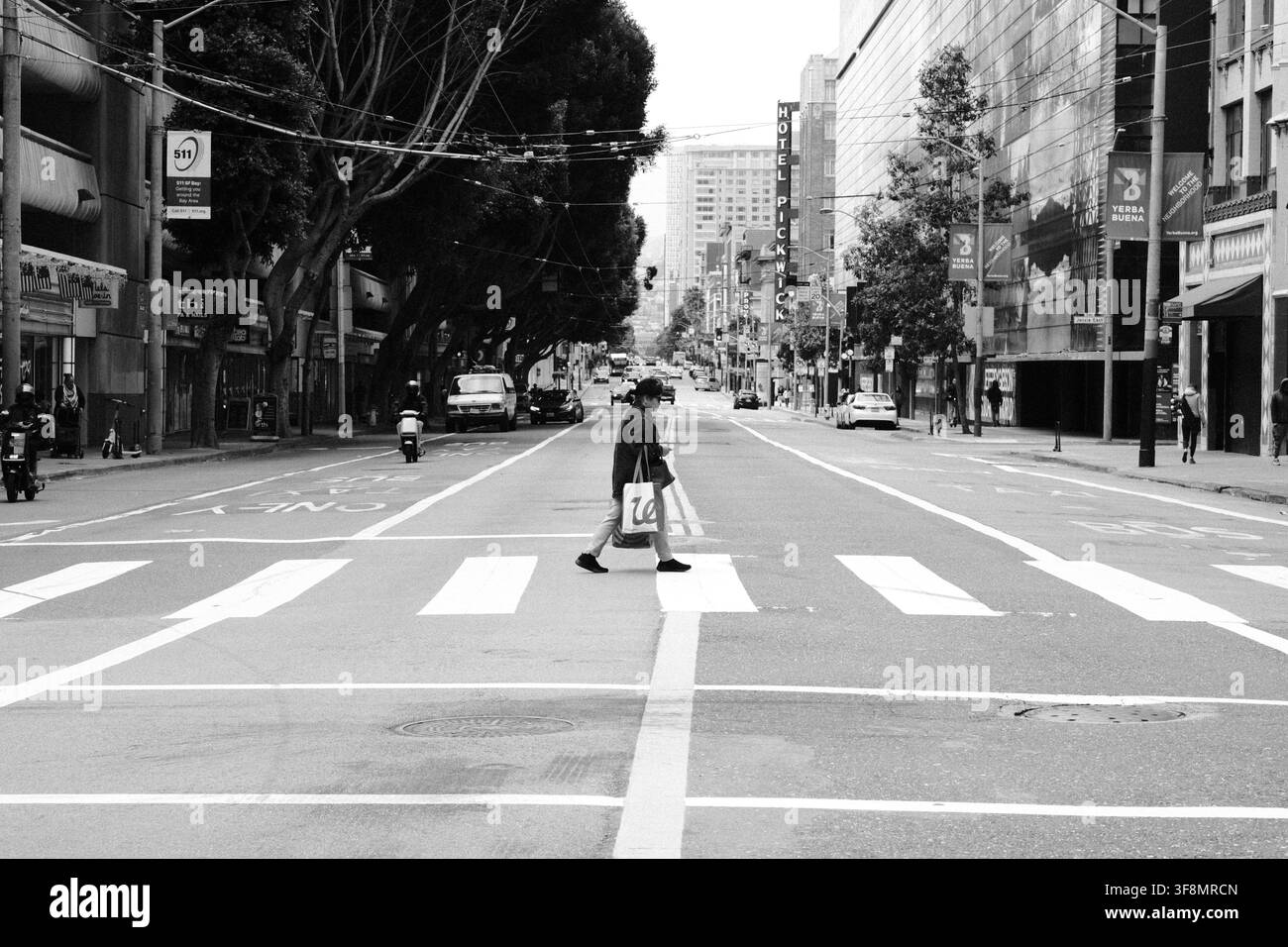 Pedone che attraversa una larga strada urbana a San Francisco, California, con edifici commerciali e traffico cittadino sullo sfondo, fotografato B&W Foto Stock