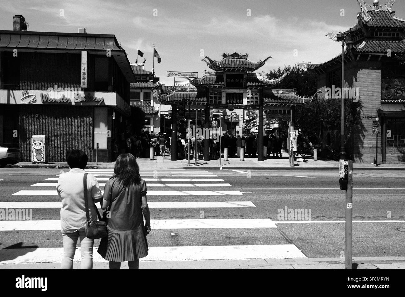 Pedoni in attesa a un passaggio pedonale di fronte all'ingresso East Gate della Central Plaza a Chinatown, Los Angeles, California, fotografata in bianco e nero. Foto Stock