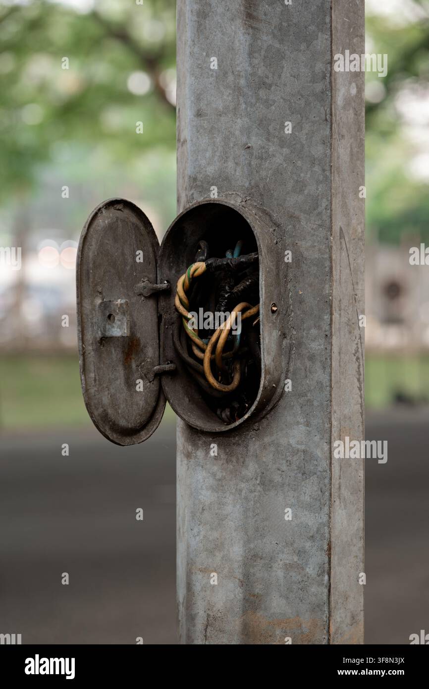 Pannello di accesso elettrico aperto su un palo di lampione metallico che espone cavi attorcigliati. Foto Stock