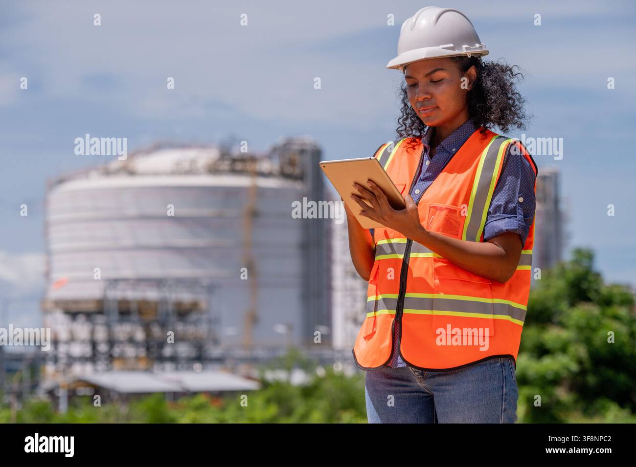 Ingegneri che indossano dispositivi di sicurezza, compresi caschi protettivi, che esaminano un tablet per il rilevamento in un'installazione industriale durante lavori di gas o raffineria di petrolio Foto Stock
