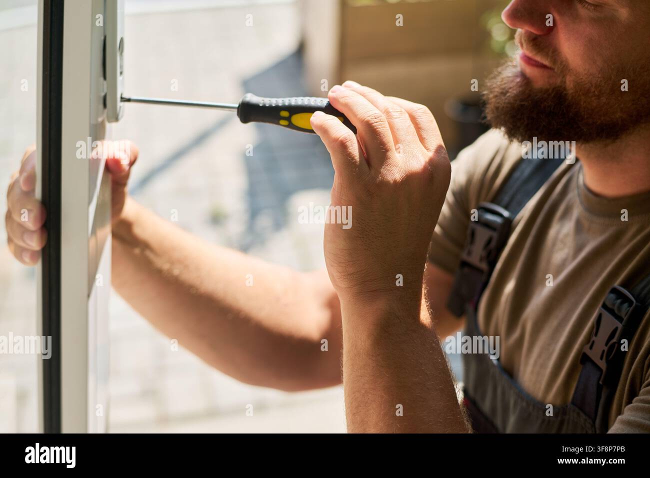 Uomo che ripara la serratura della finestra con un cacciavite durante la ristrutturazione della casa Foto Stock