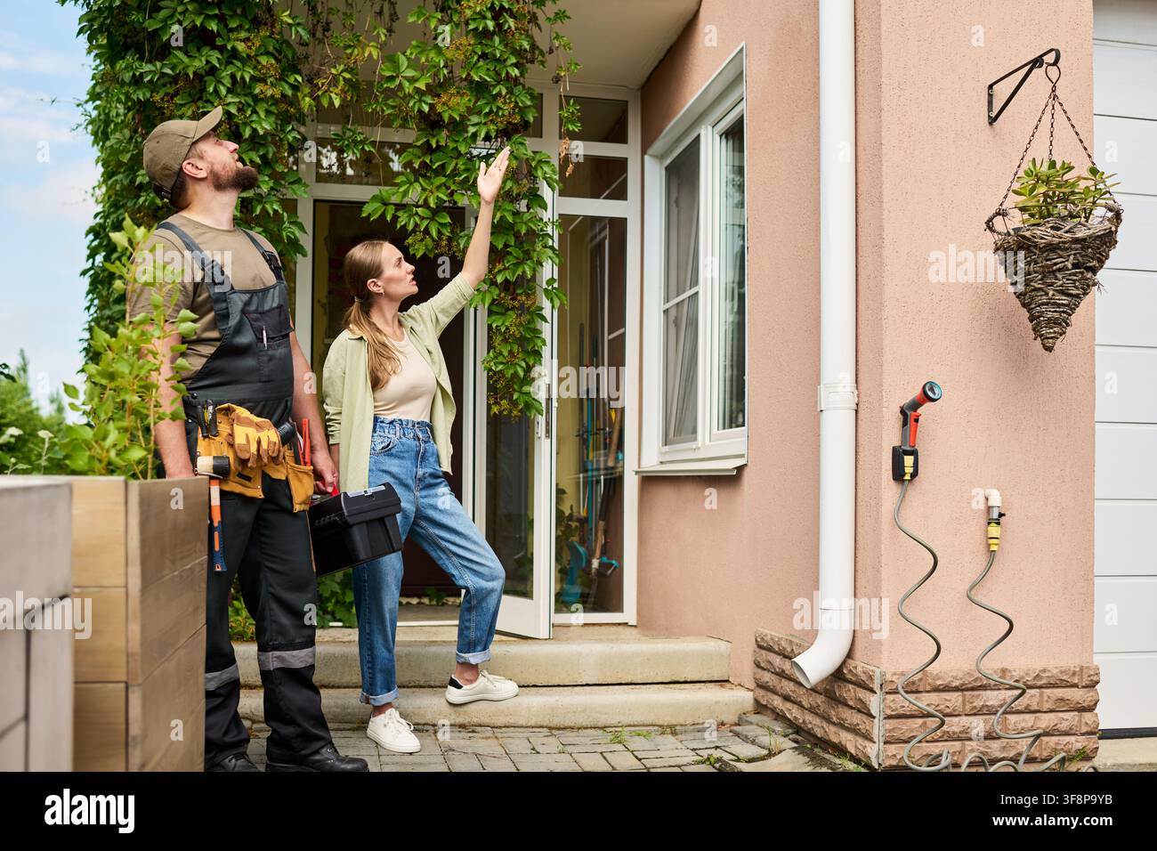 Donna che mostra i danni esterni della casa a un artigiano per la ristrutturazione della casa Foto Stock