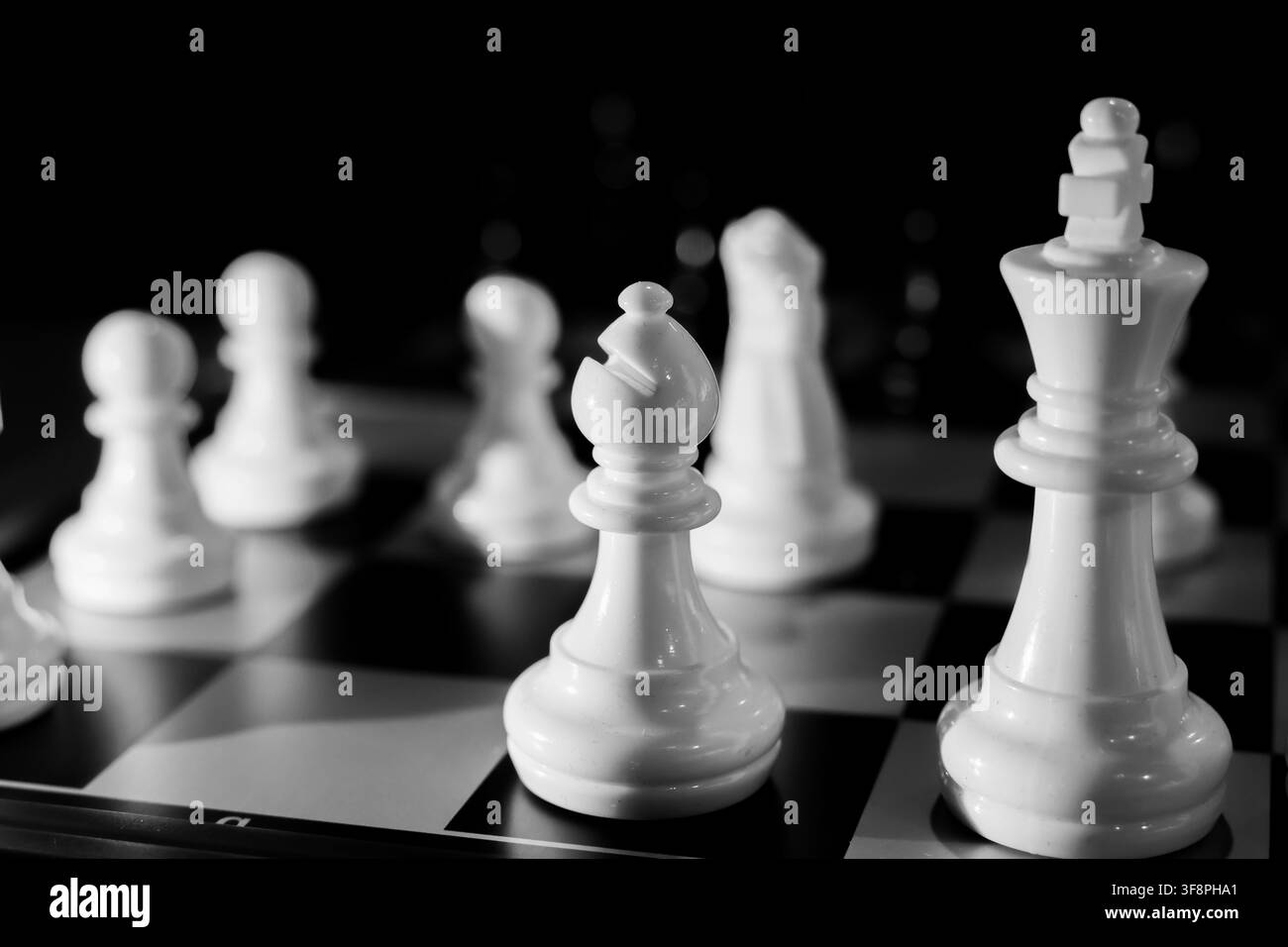 Un primo piano drammatico di pezzi di scacchi bianchi su una scacchiera bianca e nera con profondità di campo ridotta che trasmette strategia e tensione Foto Stock