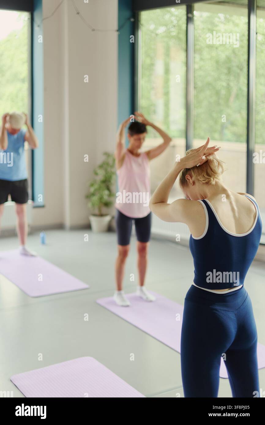 Immagine verticale di un'istruttrice di fitness caucasica che guida una classe di yoga per anziani attivi in uno studio moderno, promuovendo programmi di invecchiamento sano e benessere Foto Stock