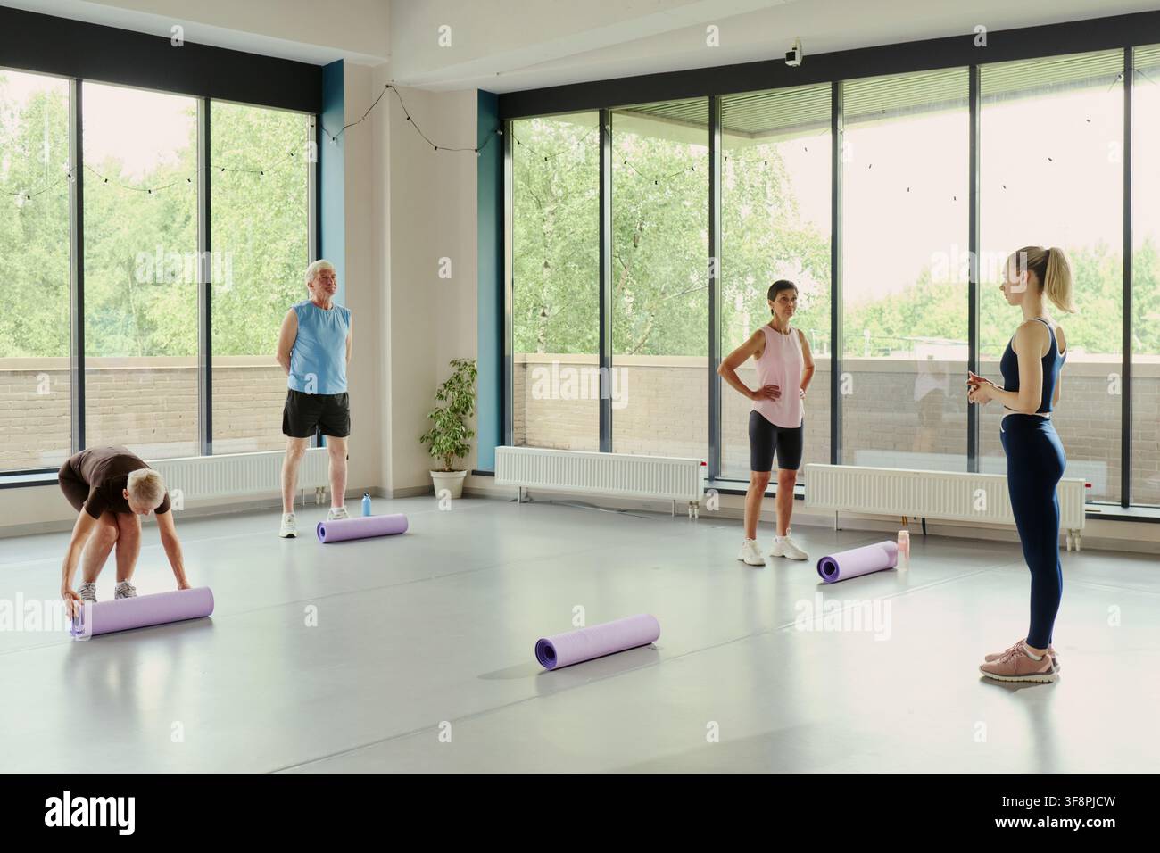 Gruppo vario di anziani e persone mature caucasiche che ascoltano una giovane istruttrice in una palestra. Immagine adatta alla promozione dell'invecchiamento attivo e dei programmi di benessere Foto Stock