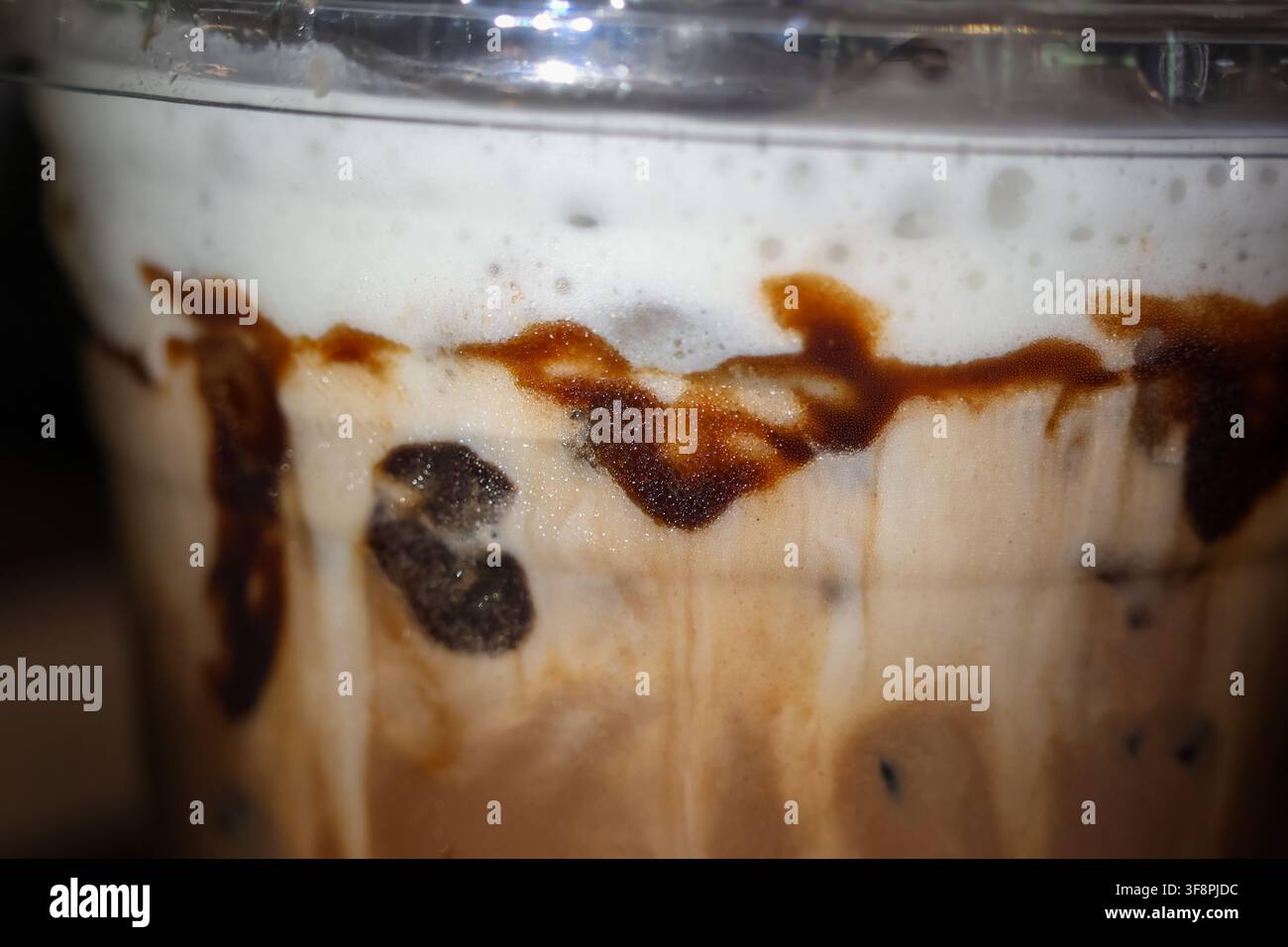 Una bevanda caffè ghiacciata con schiuma cremosa e vortice di cioccolato ricoperta di schiuma, primo piano della trama che mostra il ghiaccio che si scioglie e la ricca bevanda, indulgente col Foto Stock